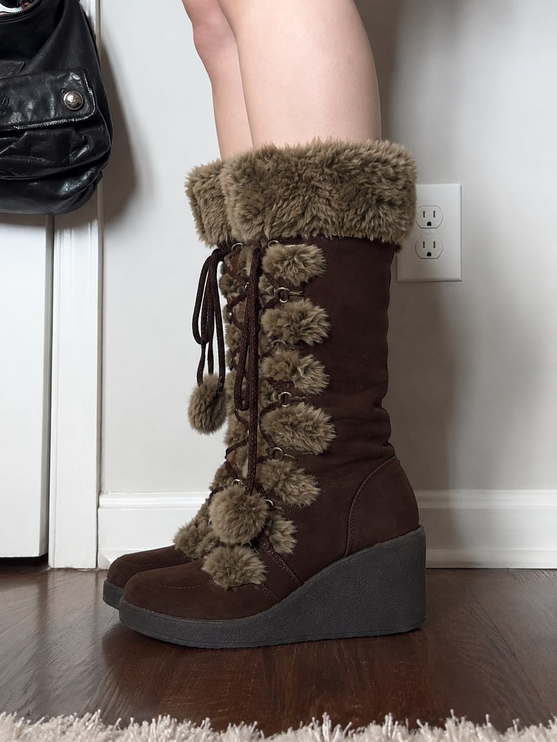 Brown suede wedge boots with faux-fur trim and laces on a person's feet.