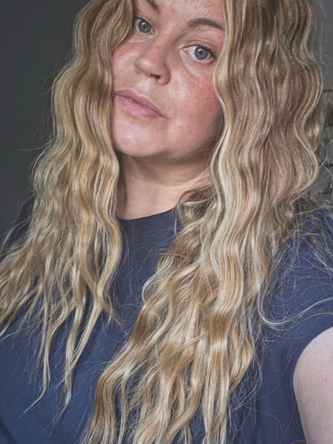 Woman with long blonde wavy hair posing against a dark grey background