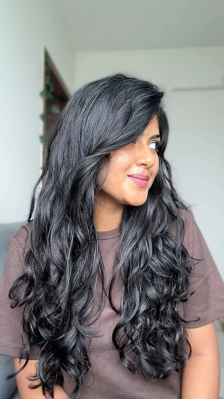 Woman with long, voluminous wavy black hair wearing a brown t-shirt.
