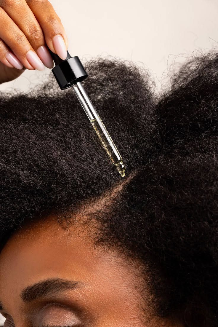 Person applying hair oil from a glass dropper to curly 4a hair scalp