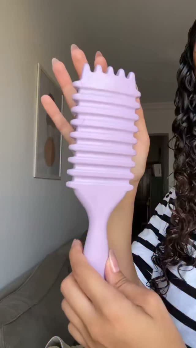 Light purple wide-tooth comb held by a person with curly dark hair.