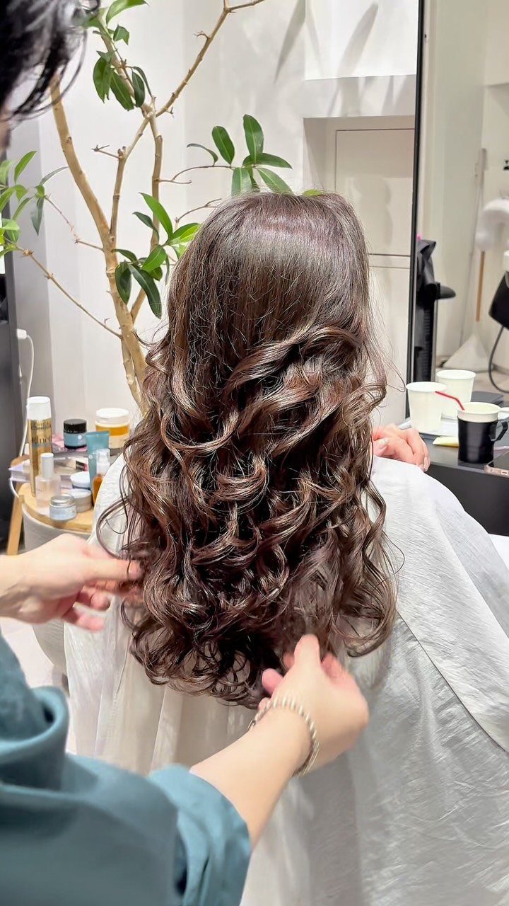 Long brown curly hair being styled by a professional in a bright salon.