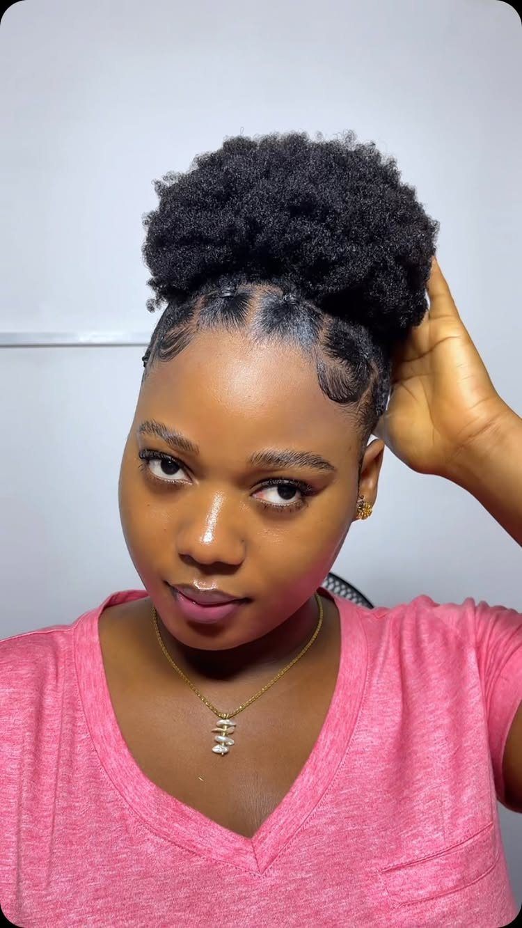 Woman with dark skin wearing a pink shirt and a high afro puff hairstyle.