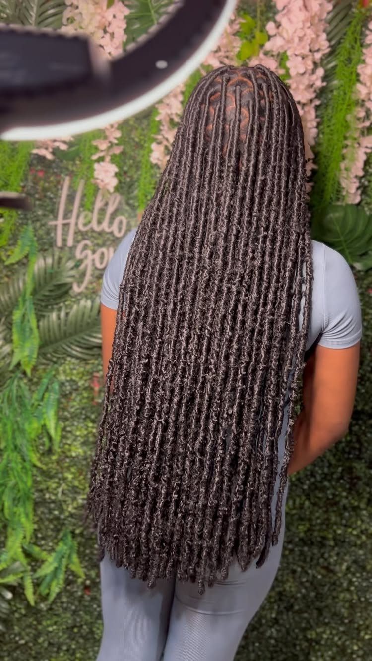 Long dark brown faux locs on a person standing before a floral wall.