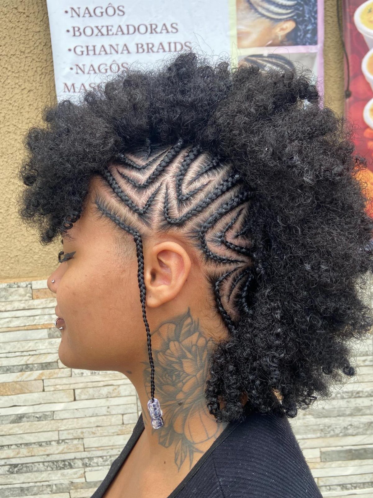 Person with a mohawk style featuring geometric cornrow braids and voluminous curly afro hair.
