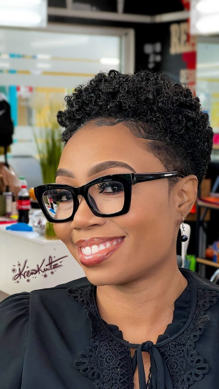 Woman with a short natural mini afro and black glasses smiling in a salon.