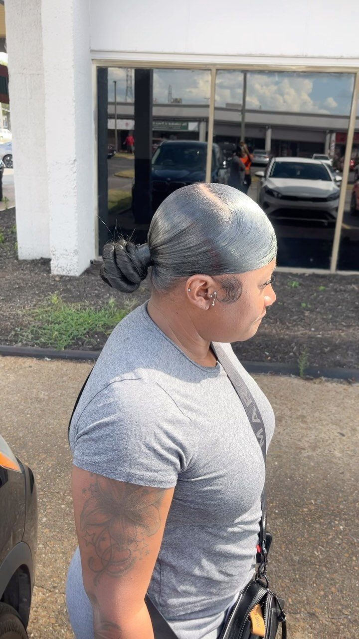 Person with sleek pulled back hair bun wearing a grey t-shirt outdoors.