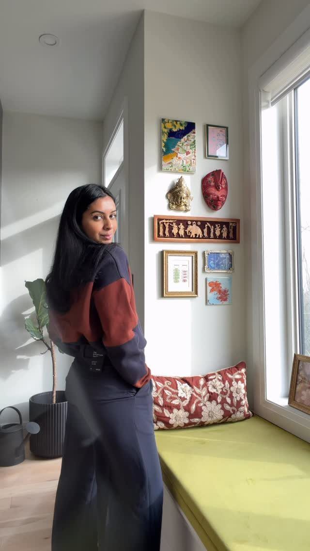 Woman wearing a color-blocked sweater and wide-leg navy trousers standing by a window.