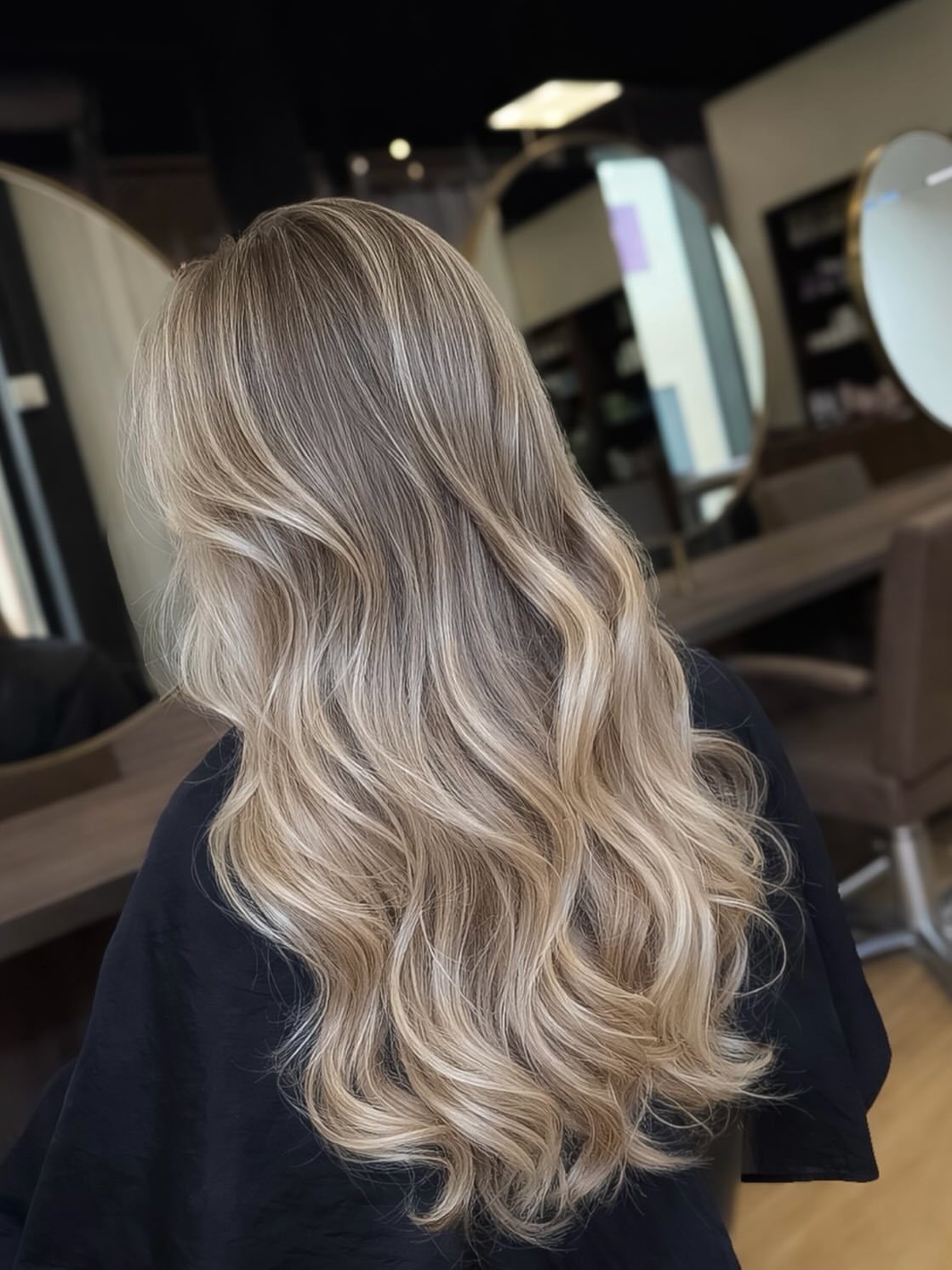 Long wavy ash blonde balayage hair with dark roots in a salon