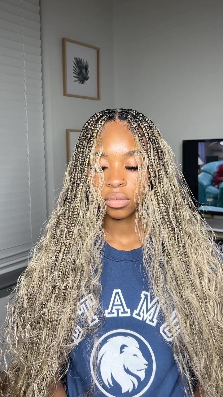 Woman with long ash blonde braids and wavy ends wearing a blue shirt.