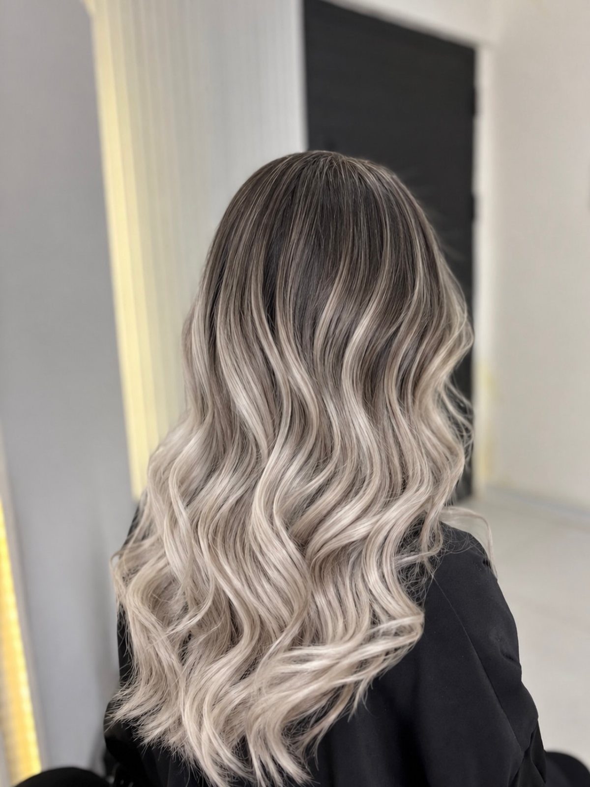 Long wavy hair with a dark brown to ash blonde ombre gradient.