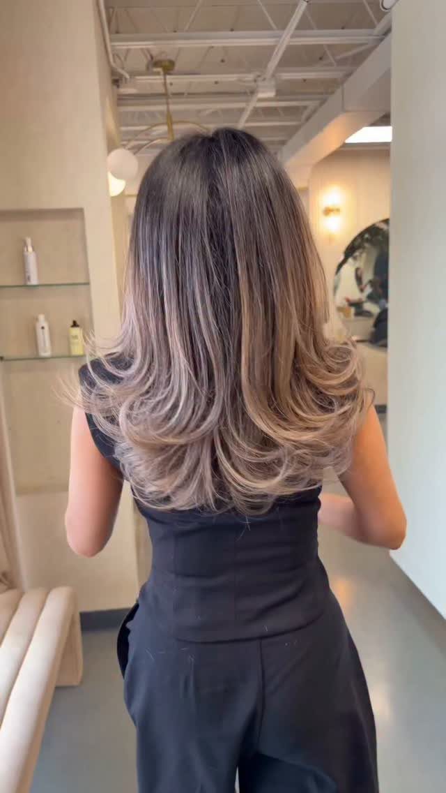 Woman with rooted blonde hair and ash blonde layers in a salon