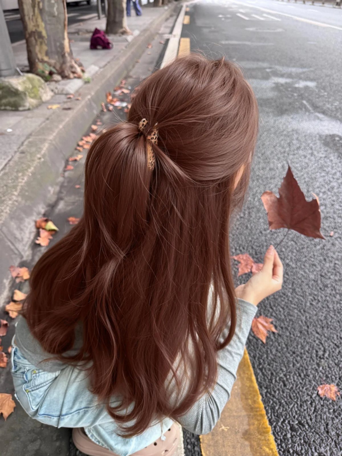 Woman with long auburn brown hair holding a fallen autumn leaf on a street