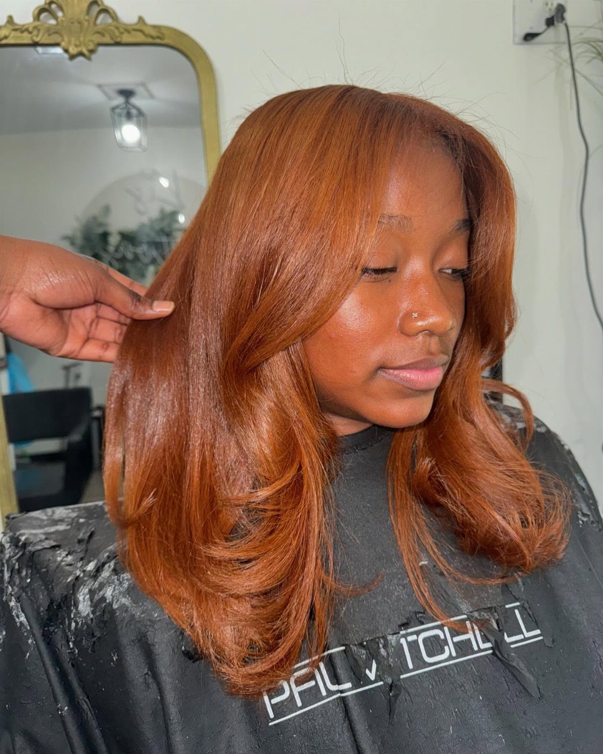 Woman with dark skin showcasing long, wavy auburn brown hair in a salon.