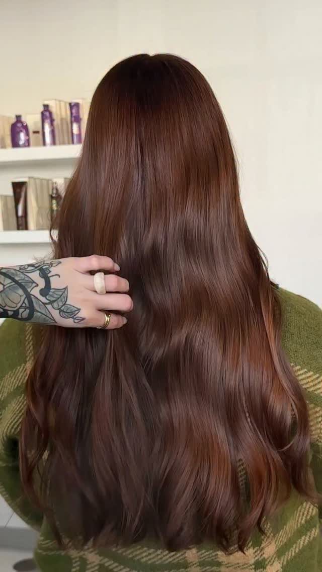 Long wavy chocolate auburn brown hair seen from behind with a tattooed hand.
