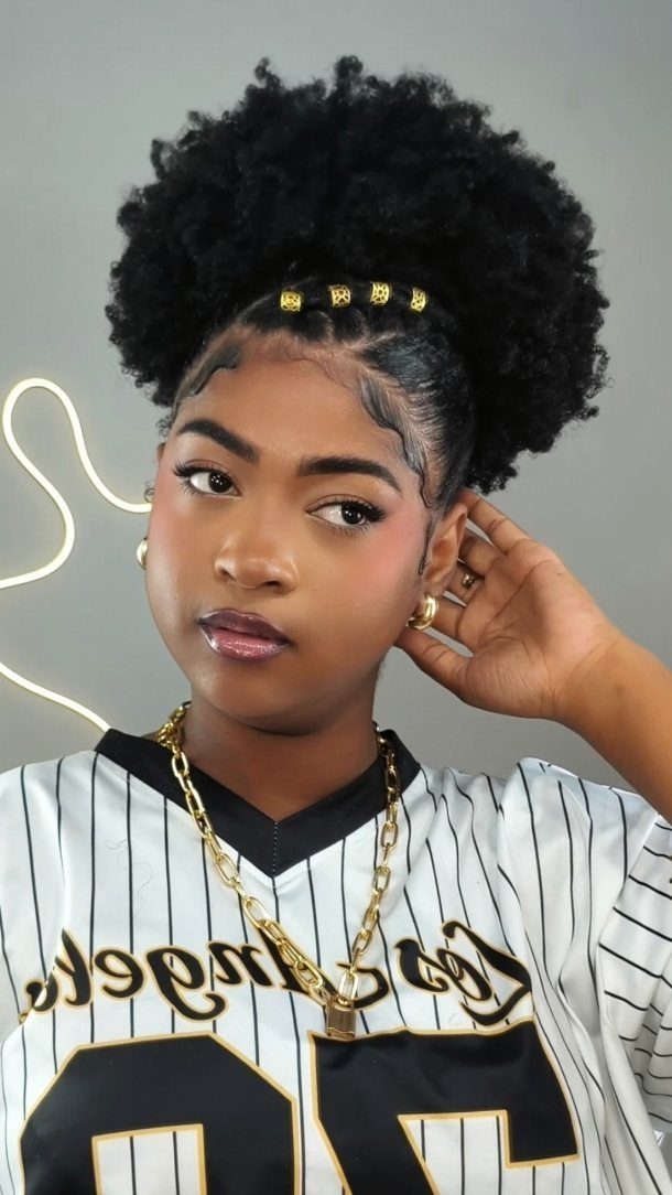 Woman with a voluminous afro puff hairstyle, gold beads, and pinstripe jersey.