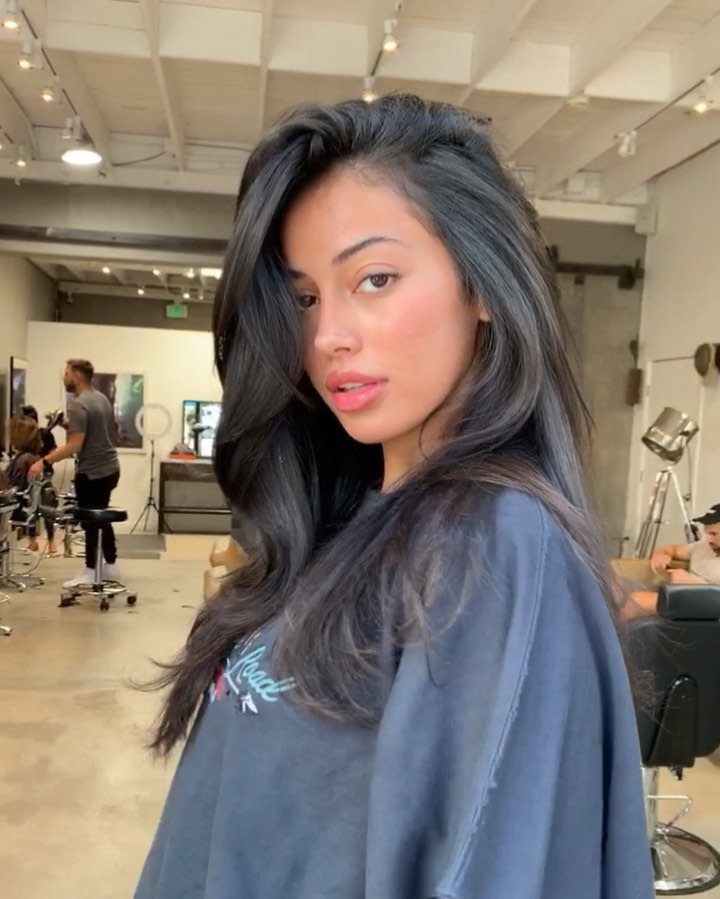 Woman with voluminous dark brown blowout hair posing in a bright hair salon.