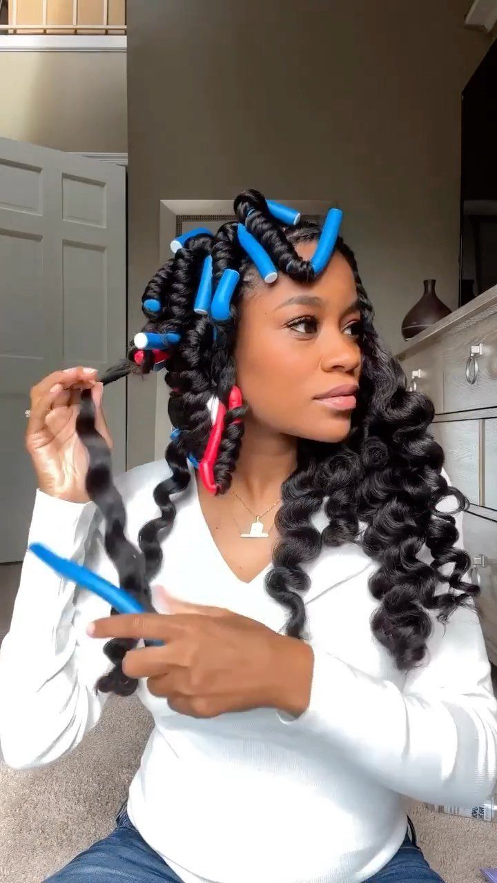 Woman with curly black hair using blue and red flexi-rod rollers for styling.