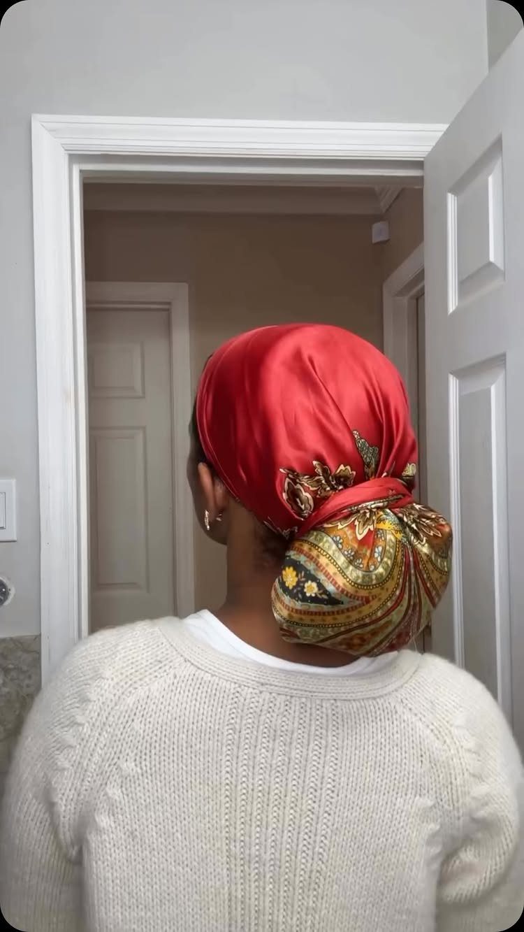 Person from behind wearing a red satin head wrap and white cable-knit sweater.