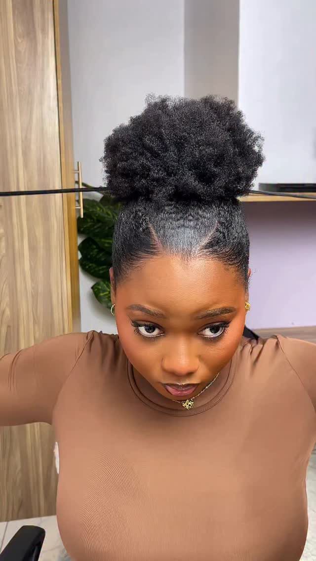 Woman with black natural hair styled in a high voluminous puff and slicked sides.