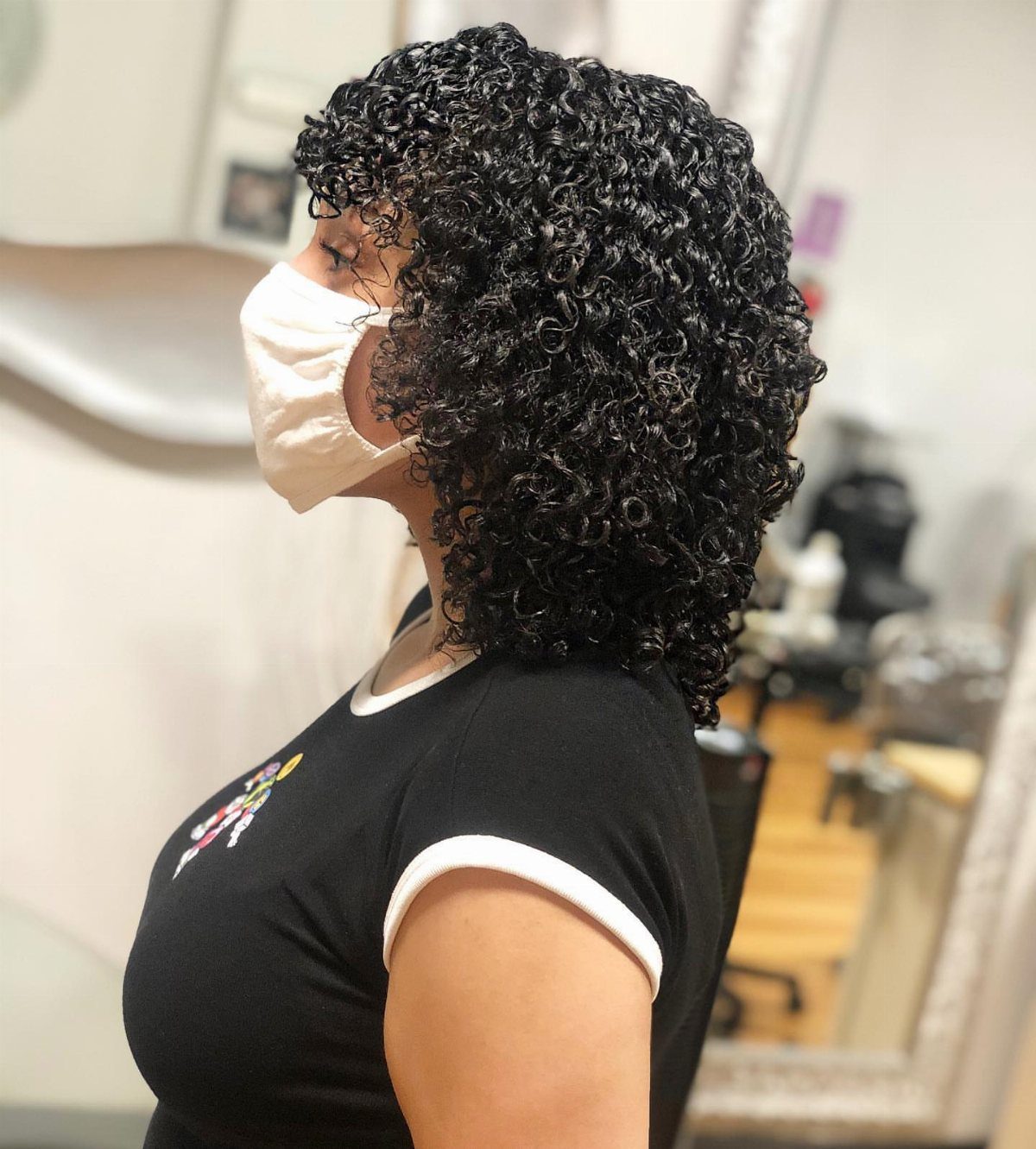 Person with voluminous curly black hair wearing a white face mask and black shirt.
