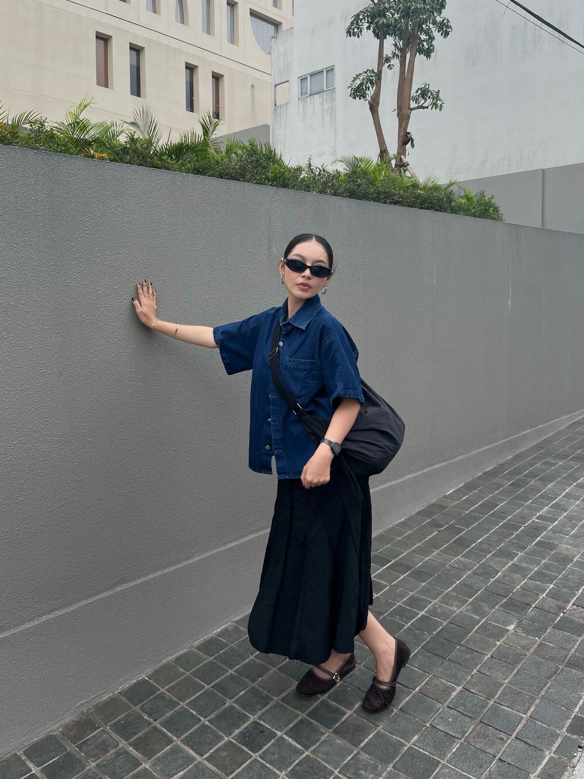Woman wearing a blue denim button-up shirt and a long black maxi skirt.