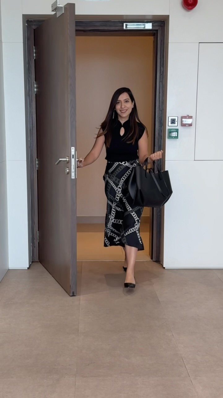 Woman in black sleeveless top and chain-print maxi skirt holding a black handbag.