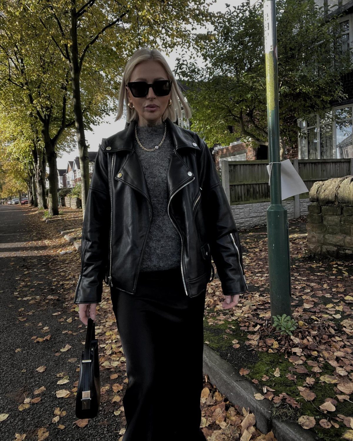 Woman in black leather jacket and black maxi skirt standing on autumn street
