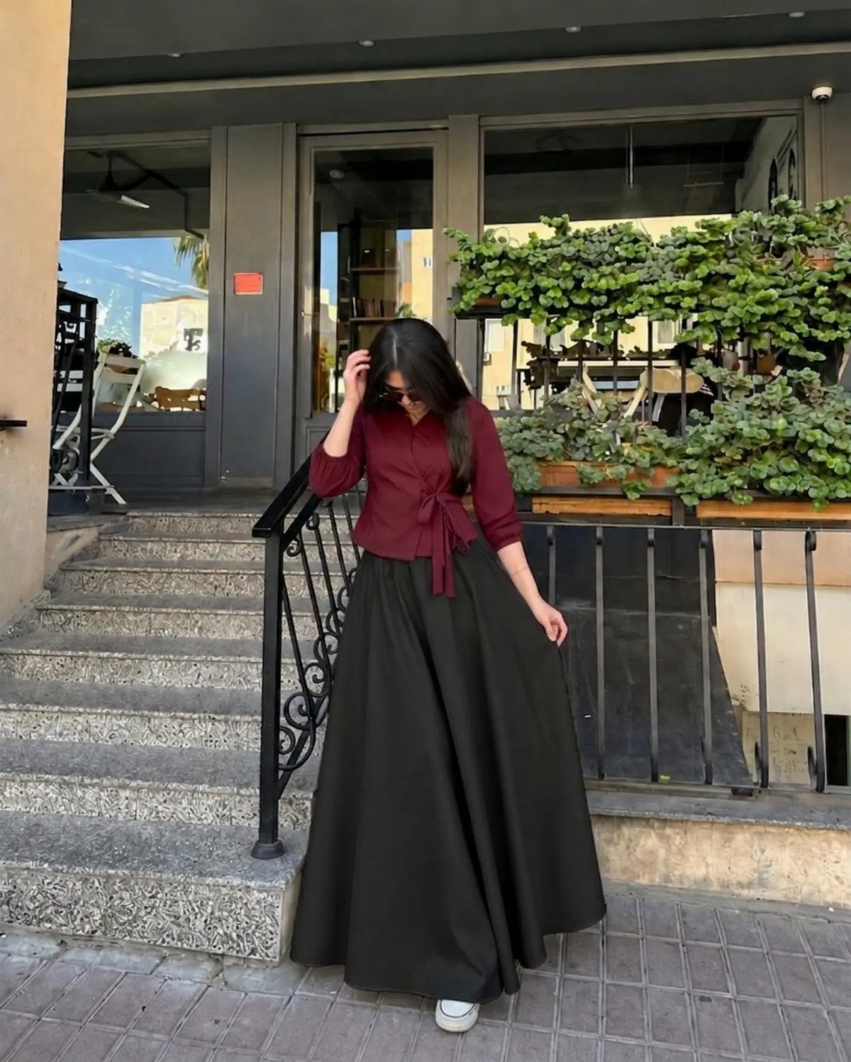 Woman wearing a black maxi skirt, maroon button-up blouse, and white sneakers outdoors.
