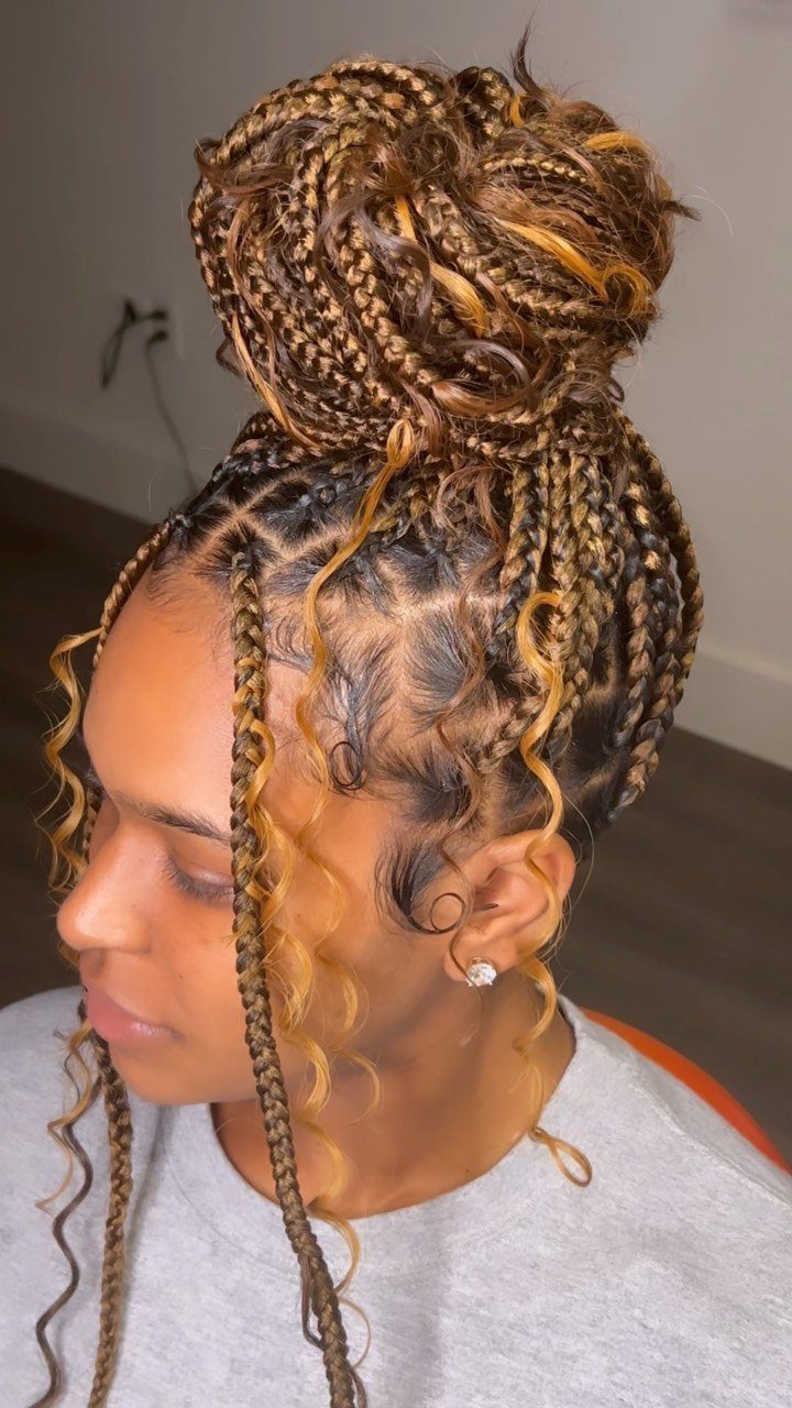 Woman with honey-blonde boho braids styled in a high bun with curly tendrils.