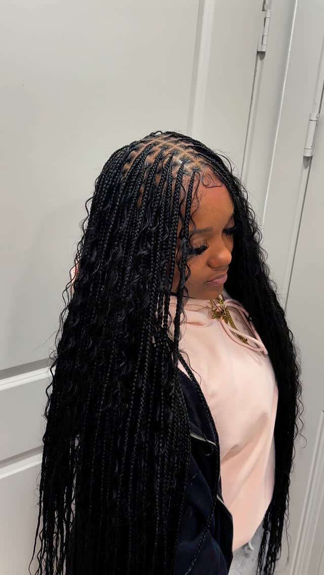 Woman with long black boho knotless braids and curly ends against white wall
