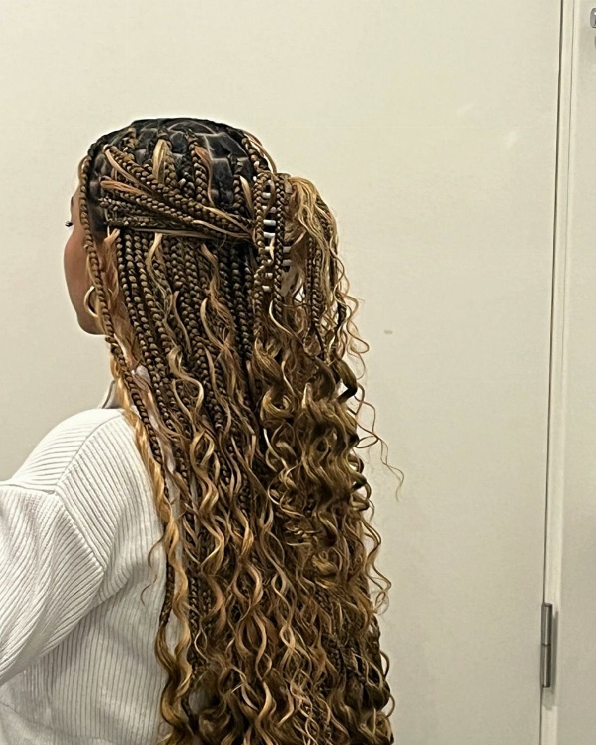 Long honey-blonde boho braids with loose curls cascading down a woman's back.