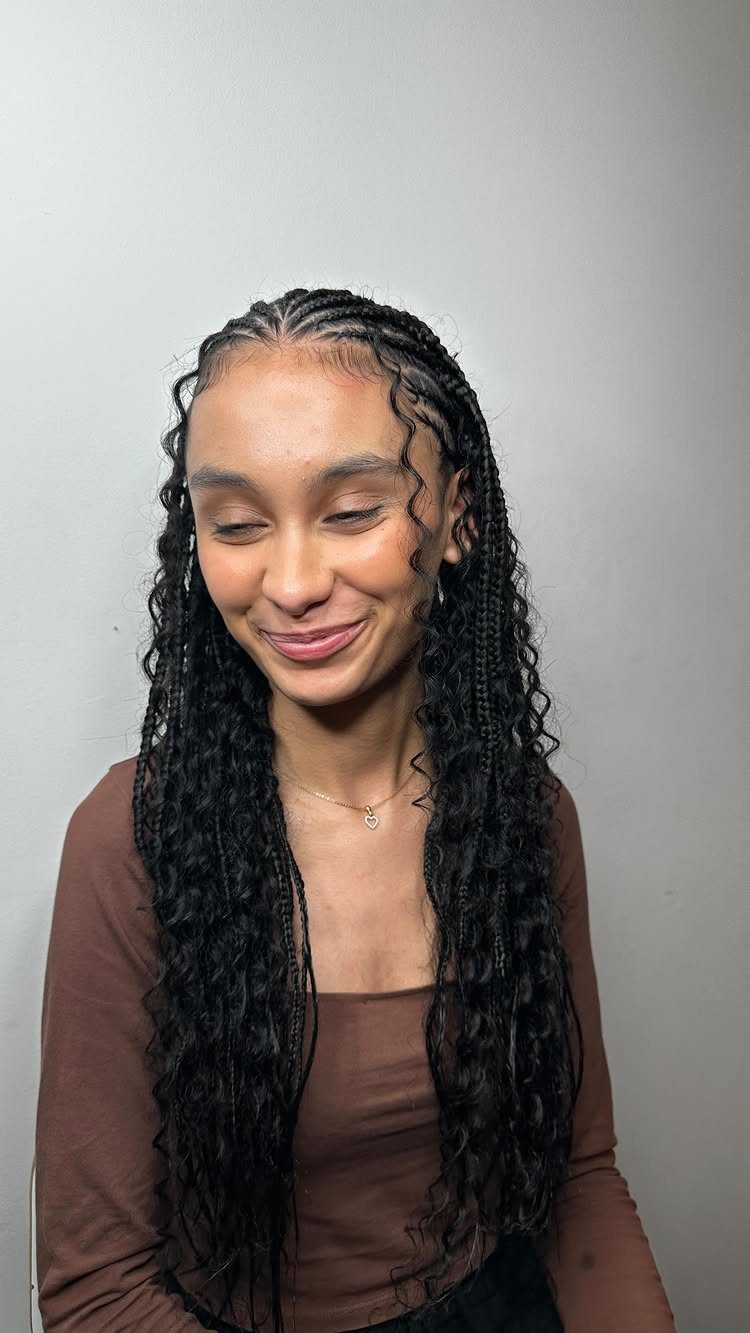 Woman with small black boho braids and curly tendrils wearing a brown top.