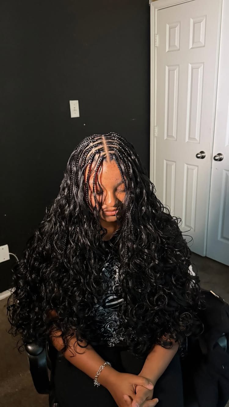 Person with long thin jet-black braids and voluminous curls against a dark background