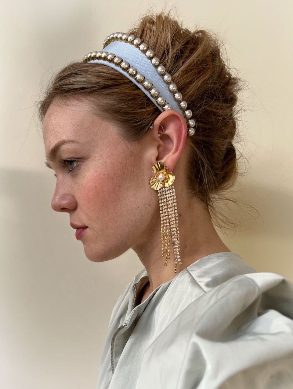 16 Bun Hairstyles for Homecoming: Updos, Braids and More 9 Woman with a textured bun wearing a light blue double-pearl headband and gold earrings.