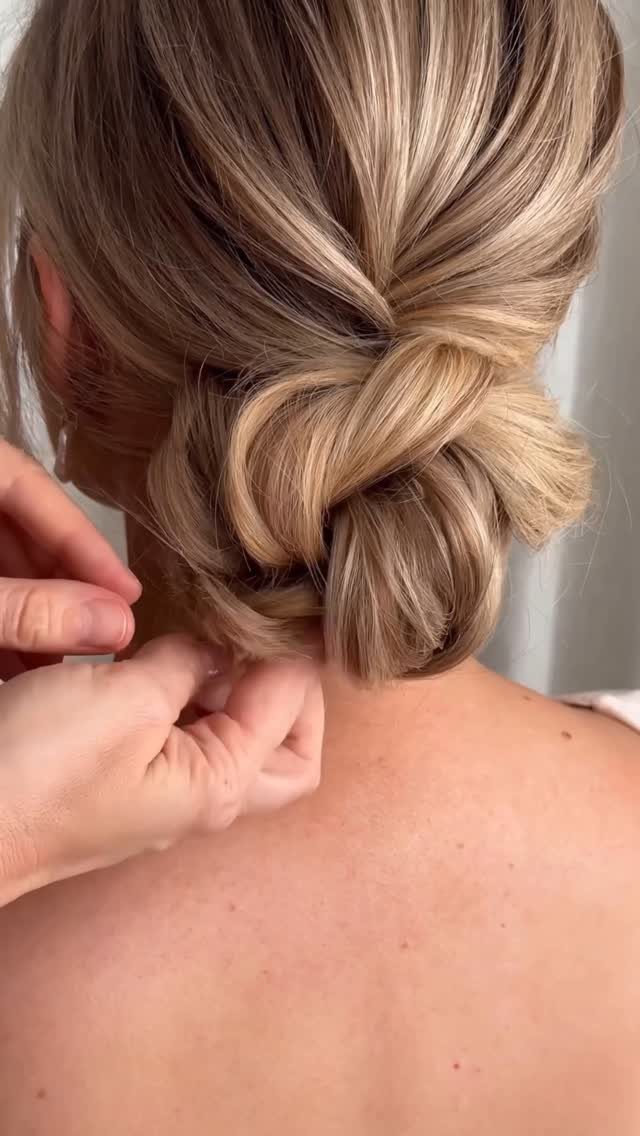 16 Bun Hairstyles for Homecoming: Updos, Braids and More 13 Blonde hair styled in a low knotted bun being adjusted by hands.