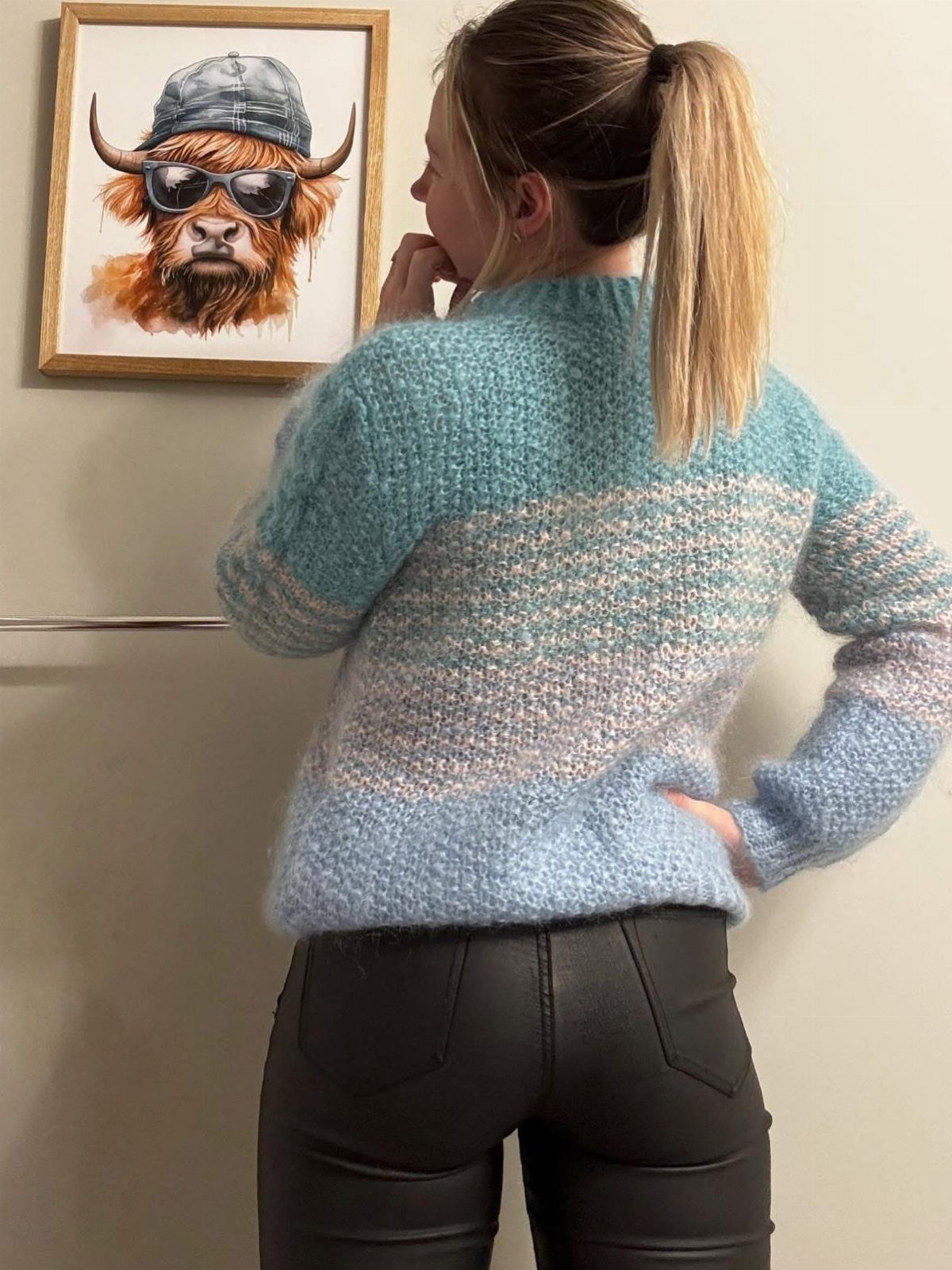 Woman wearing a blue striped knit sweater and black leather pants from behind.