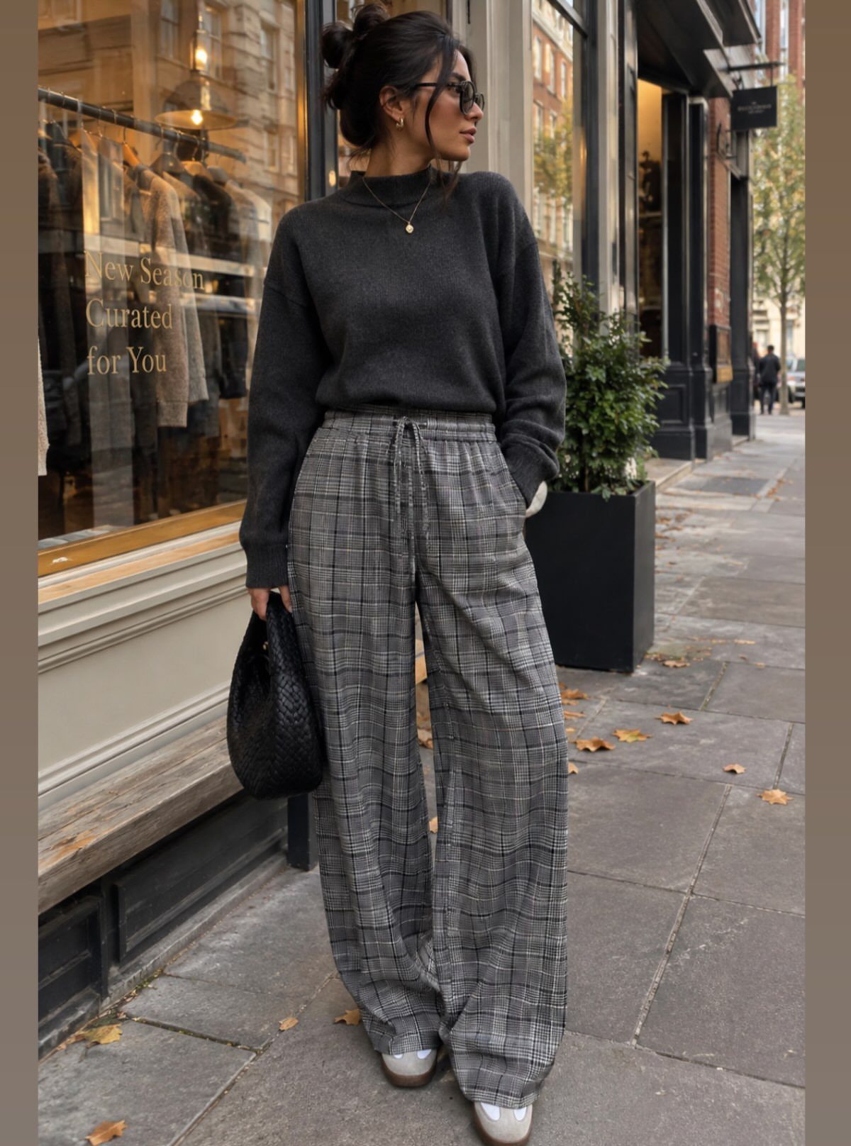 Woman wearing a grey sweater and wide-leg plaid trousers on a city street.
