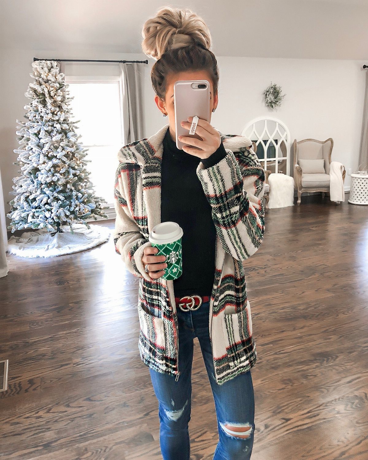 Woman in a plaid cardigan, black turtleneck, and distressed blue jeans holding coffee.