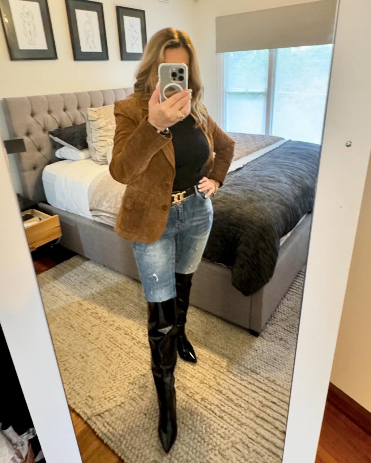 Woman wearing a brown blazer, blue jeans, and black pointed-toe tall boots.