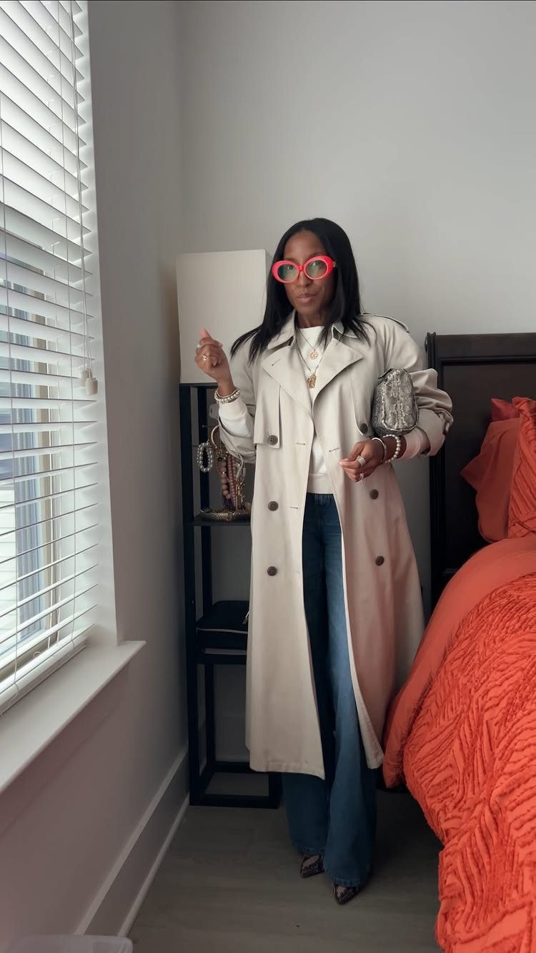 Woman wearing a long beige trench coat and wide-leg blue jeans indoors.
