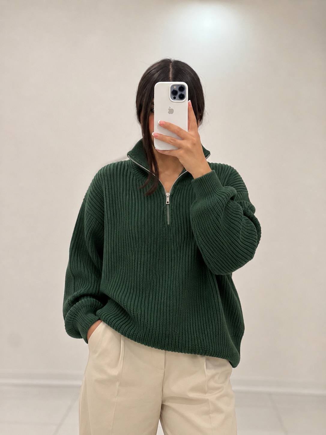 Person wearing a dark green quarter-zip ribbed knit sweater and cream trousers.