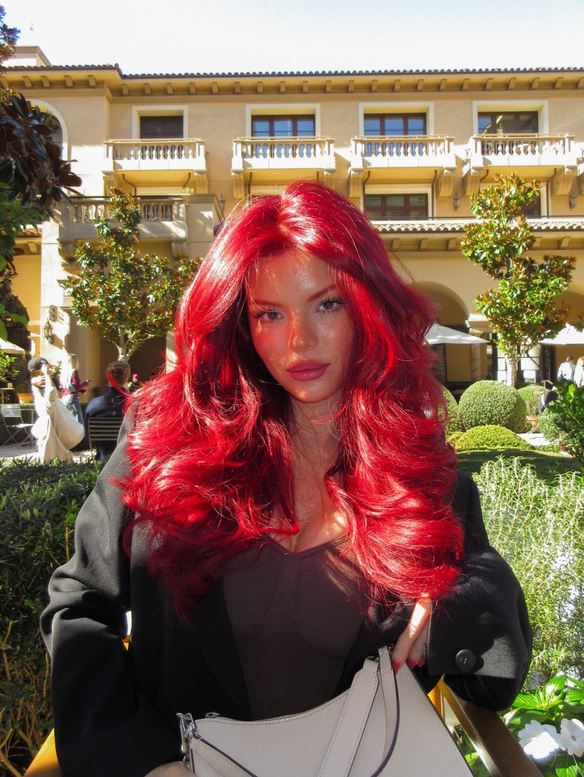 Cherry Red Hair Aesthetic: 7 Ideas for Every Length 2 Woman with voluminous cherry red curls posing in front of a sunny building.