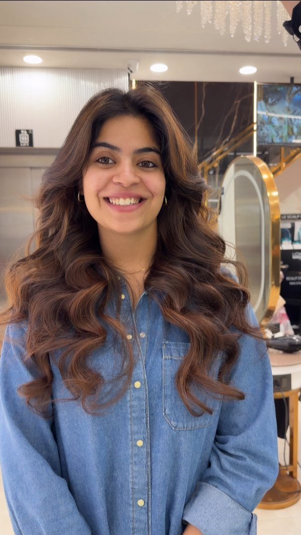 Woman with long wavy dark brown hair and warm caramel highlights smiling.