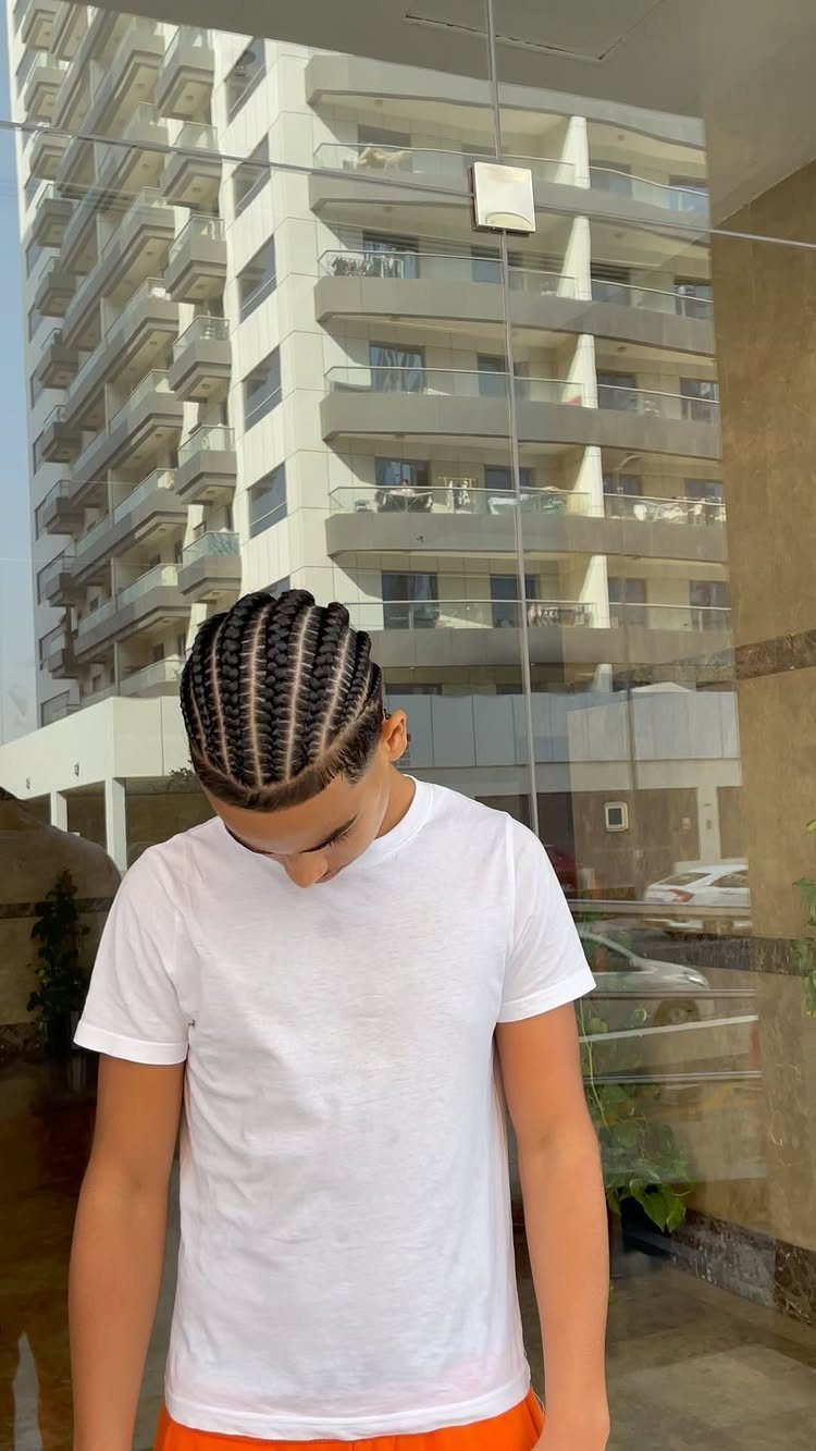 Man with straight-back cornrow braids wearing a white t-shirt in front of a building