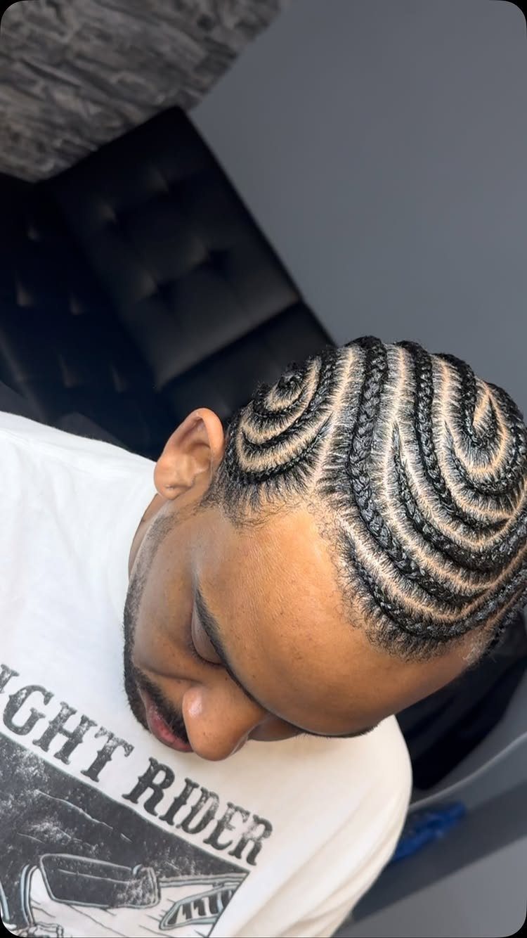 Man with intricate curved cornrow braids in a swirling pattern on his head.