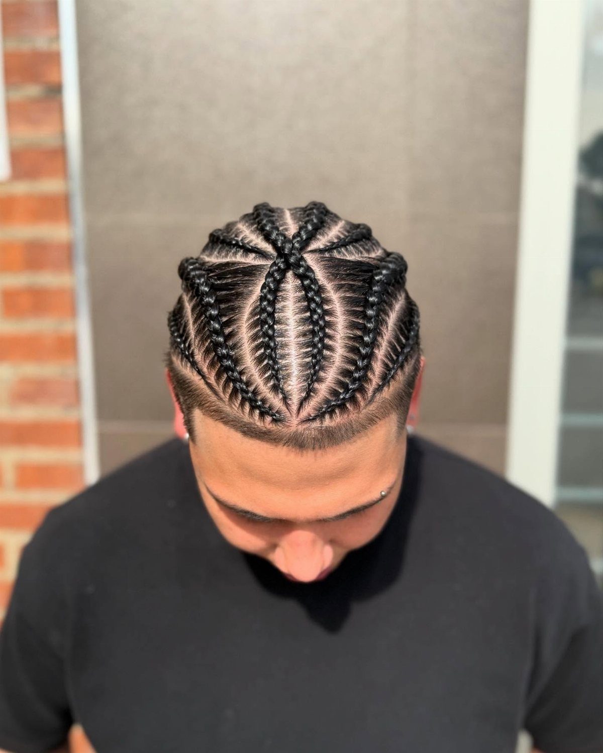Man with intricate cornrow braids radiating from the center of his head.