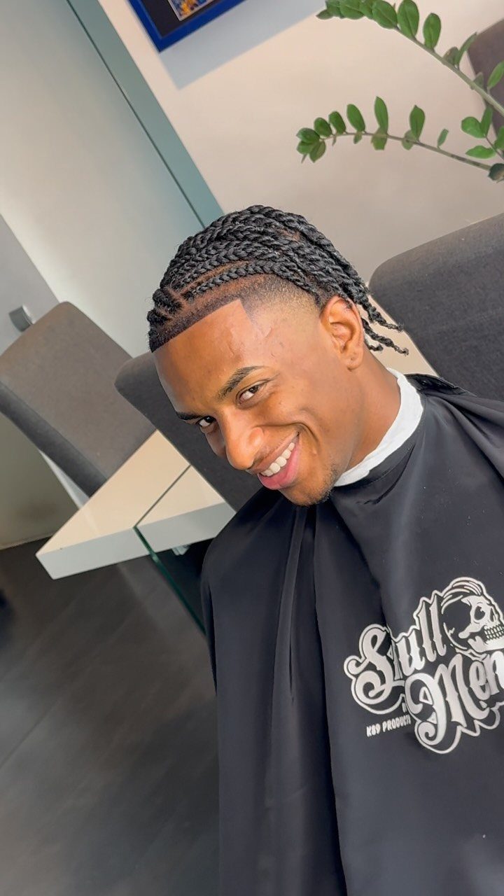 Man with straight-back cornrow braids and a clean taper fade smiling in barber shop