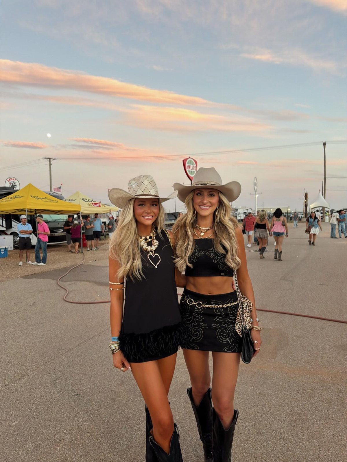 Two women in black Western outfits and cowboy hats posing at a festival.