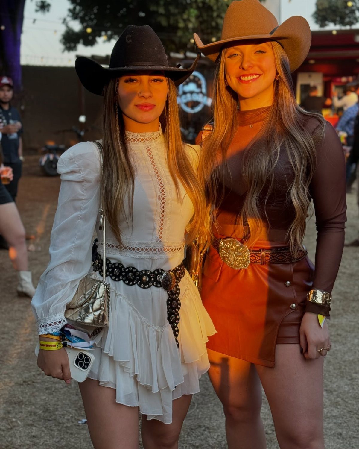Two women wearing cowboy hats and western-style mini dresses at an outdoor festival.